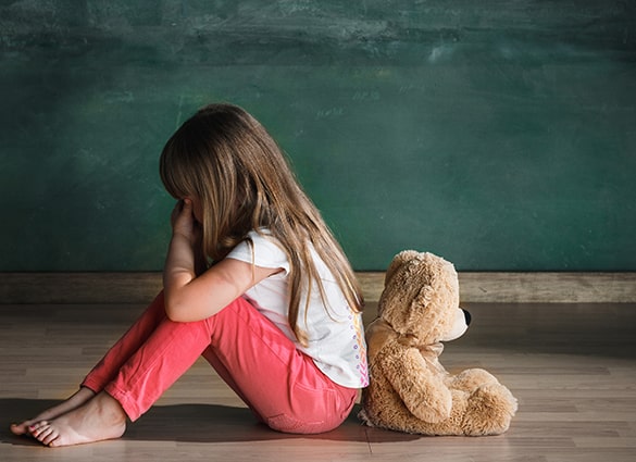 Little-girl-with-teddy-bear-sitting-on-floor-in-empty-room.-Autism-concept
